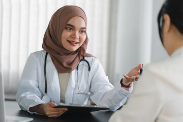 Young muslim female doctor in brown hijab headscarf having appointment consulting female patient in...