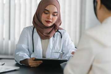 Woman patient visiting muslim female doctor at clinic office. Muslim female doctor writes a...