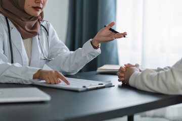 Young muslim female doctor in brown hijab headscarf having appointment consulting female patient in...