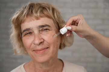 Close-up portrait of an old woman applying hyaluronic acid serum with a pipette. Anti-aging face...