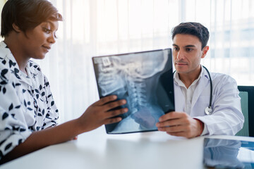 Male doctor in white medical uniform explaining x-ray results to female patient on consultation. They Consult Digital Tablet Computer while Talking about Patient's Health.
