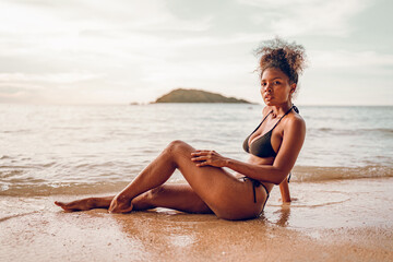 Beautiful African american woman in pink bikini on tropical beach. Portrait of dark skinned woman smiling at sea. Brunette tanned girl in swimwear enjoying and walking on beach. - obrazy, fototapety, plakaty