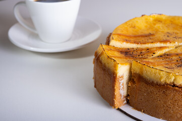cheese cheesecake with a crust, cut into a piece, on a light dish, background, with a cup of coffee. Preparation of cakes and pastries