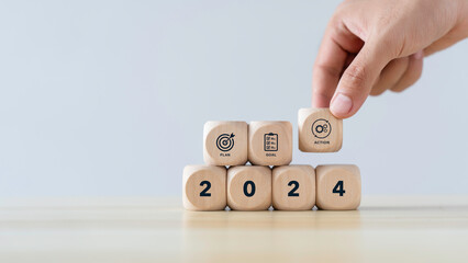 Happy New Year 2024 concept. Hand-place wooden cubes with 2024 and the goal icon on a white background for planning new projects The annual plan for Business to targets, goals, and action. - obrazy, fototapety, plakaty