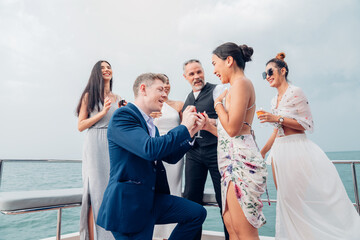 Happy man make surprise proposal of marriage to girlfriend on Yacht. Attractive romantic male proposing to beautiful happy woman with wedding ring enjoying surprise engagement together. - obrazy, fototapety, plakaty