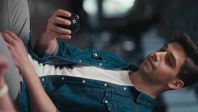 Vertical video of a brunette man in a blue denim jacket passing a black ball to another group therapy participant. Expressing your opinion and introducing yourself while passing the ball to each other