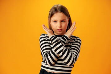 Teen girl shows cross hands gesture, rejecting something over yellow background in studio