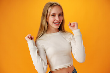 Portrait of a joyful happy teenage girl celebrating success on yellow background