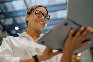 Stylish business woman in eyeglasses working on laptop standing on modern office background 