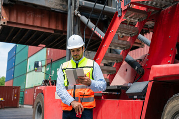 Fototapeta premium Male Industrial Engineer in White Hard Hat using digital tablet checking container at container yard warehouse. Logistics business.