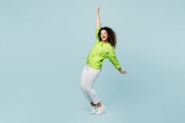 Fototapeta na wymiar Full body young latin woman wear green shirt casual clothes stand on toes leaning back with outstretched hands isolated on plain pastel light blue cyan background studio portrait. Lifestyle concept.