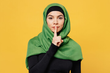Young asian muslim woman wear green hijab abaya black clothes say hush be quiet with finger on lips...