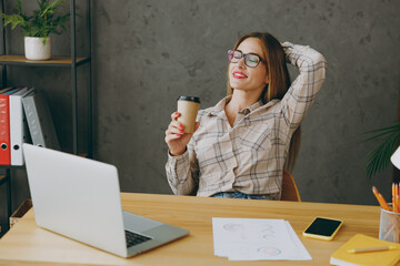 Young relaxed employee business woman wear shirt casual clothes glasses sit work at office desk...