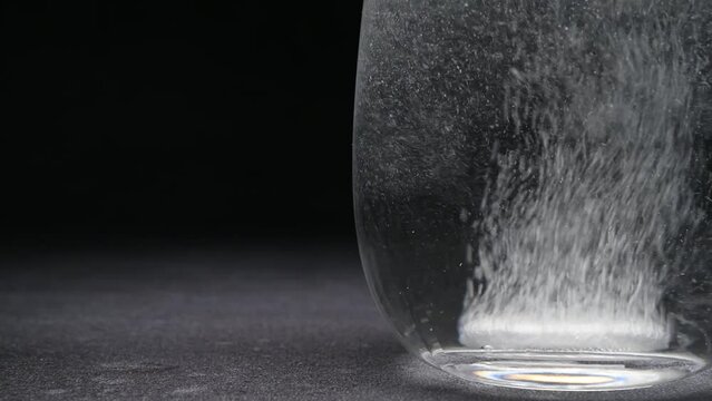 Effervescent tablet in transparent glass cup on dark background, close-up, space for text.	