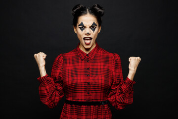 Young woman with Halloween makeup face art mask wear clown costume red dress do winner gesture celebrate say yes isolated on plain solid black background studio portrait. Scary holiday party concept.