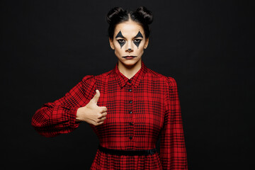 Young serious woman with Halloween makeup face art mask wear clown costume red dress showing thumb...