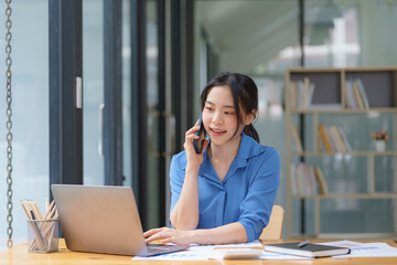 Obraz premium Beautiful businesswoman using a smartphone and working with a laptop while sitting at an office desk, working from home concept.