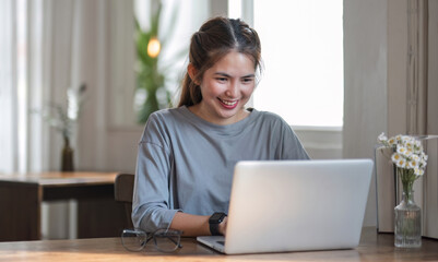 Freelance business women casual wear using laptop working call video conference with customer in workplace in living room at home. Happy young Asian girl relax sitting on desk do job in internet.