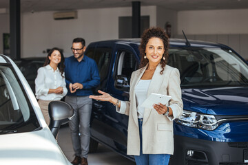 Smiling saleswoman holding document while looking at camera at car showroom. Cardealer holding...