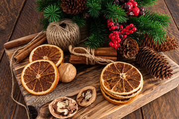 Dried orange slices, walnuts, cinnamon sticks, green spruce branches on a wooden podium and a rustic table. New year christmas concept.