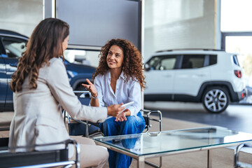 Saleswoman and a female customer in a car dealership. Sales manager explaining looking at clipboard...