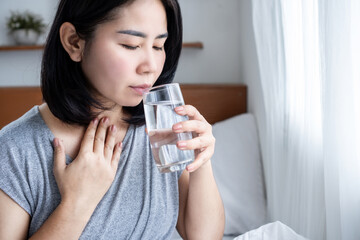 Asian woman suffering from sore throat drinking a glass of warm water in the morning