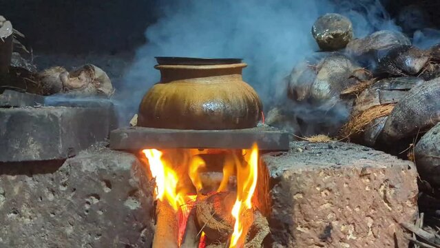 an old, traditional cooking pot under heat in a firewood stove made of mud and stone burning with smoke 