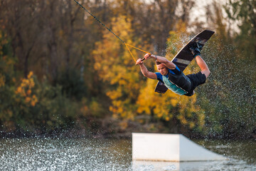An athlete does a trick from a springboard. A rider jumps on a wakeboard against a background of a...