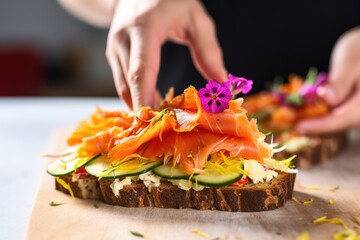 close-up of fingers placing smoked salmon on an open-faced sandwich - obrazy, fototapety, plakaty