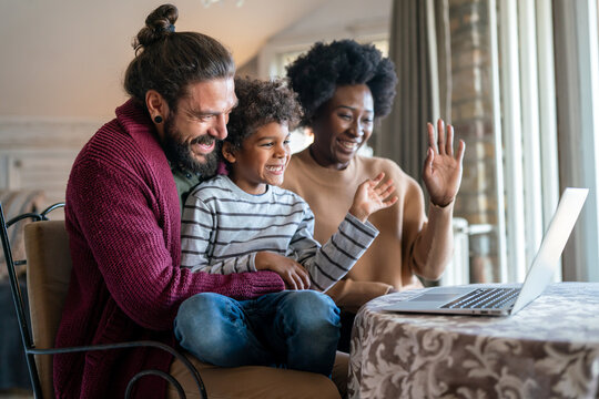 Happy multiethnic diverse family gathering around notebook and having fun during a video call