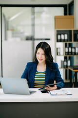 Fototapeta premium Young beautiful woman typing on tablet and laptop while sitting at the working white table office