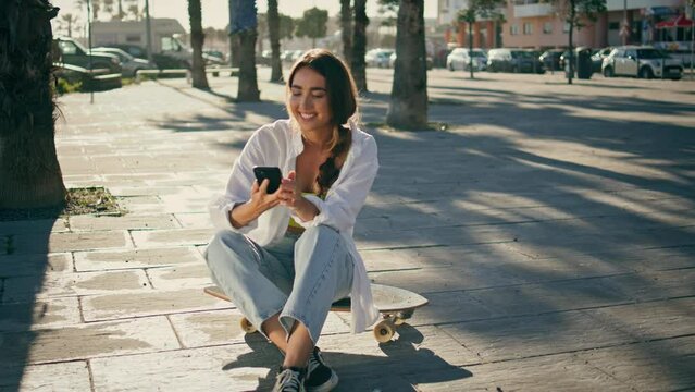 Carefree skater making selfie phone at sun alley. Sporty woman sitting longboard