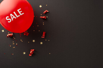 Shop smart on Black Friday with top-down view of red "sale" balloon, festive serpentine, and sparkling star-shaped confetti on black background for promo text