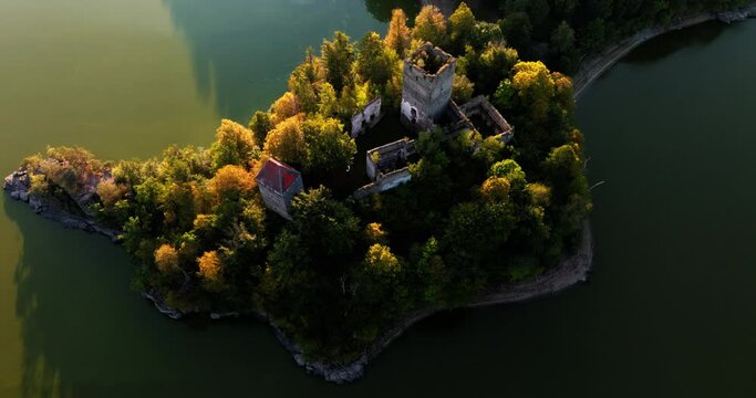 Aerial overview of incredible Ottenstein castle in middle of reservoir, golden glow illuminates autumn yellow trees