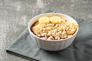 natural açaí with banana slices and oatmeal in a bowl over wooden table. top view