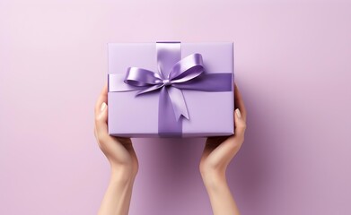 Female hands holding a purple gift box with a bow against pastel background.