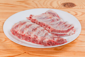 Raw pork ribs on white dish, side view close-up