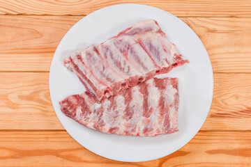 Raw pork ribs on white dish, top view