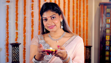 An attractive female wearing colorful jewelry holding a well-lit Diya for Diwali. Pretty lady in a...