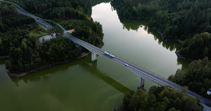 Cars and semi trucks cross over bridge spanning green river and lush forest