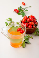 Cup with rosehip drink, bowl with rosehip berries, rosehip branches, berries in a wooden spoon on a light background.