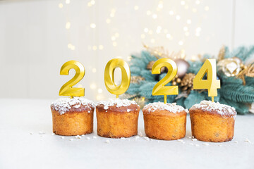 Golden candles with 2024 number on top of cupcakes with Christmas decoration and bokeh lights on...