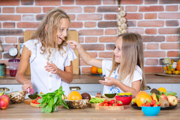 Two little girls in the kitchen with fresh vegetables. Healthy food concept. Happy sisters.