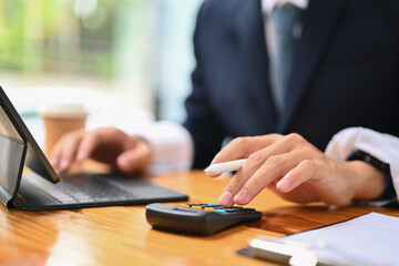 Close up male accountant analyzing sales statistics data on digital tablet and using calculator at working desk