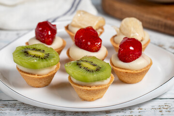 Fruit tartlets. Strawberry, banana and kiwi tartlets on a plate. snack sweet food. Close up