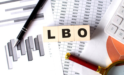 Leveraged Buyout - LBO text on wooden block on graph background with pen and magnifier