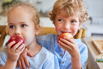 Smiling siblings eating apples at home