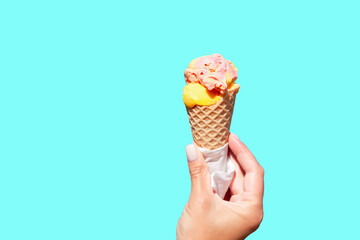 Ice cream cone in the hand against blue background. Female hand holding ice cream cone. Vanila ice cream.