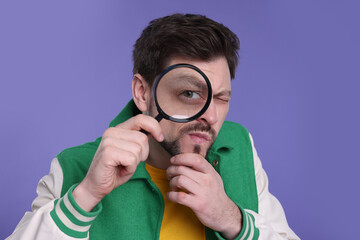 Confused man looking through magnifier glass on purple background
