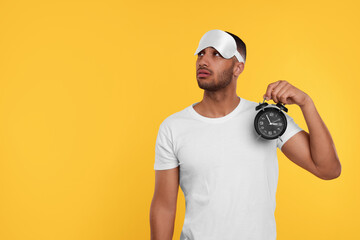 Tired man with sleep mask and alarm clock on orange background, space for text. Insomnia problem - obrazy, fototapety, plakaty
